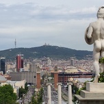 Statue overlooking a panoramic view of barcelona with the cityscape and mountains in the distance.