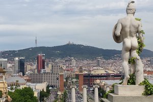 Statue overlooking a panoramic view of barcelona with the cityscape and mountains in the distance.