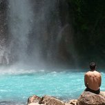 A person sitting on rocks observing a waterfall.