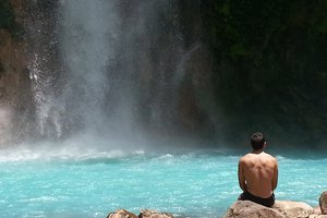 A person sitting on rocks observing a waterfall.