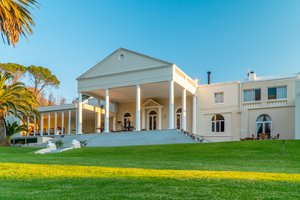 Large neoclassical-style home with a spacious lawn and palm trees during daylight.