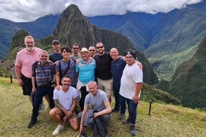 A group of men posing for a photo in front of the mountainous landscape of machu picchu.