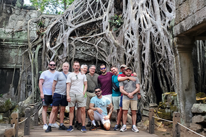 A group of tourists posing in front of an ancient temple overgrown with large tree roots.