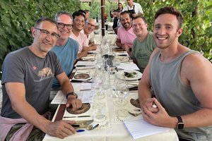 A group of people sitting at a table in a vineyard.