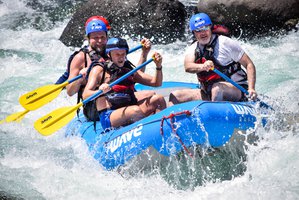 Four individuals wearing life vests and helmets white water rafting on a turbulent river.