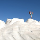 Person standing on white rock formation against a blue sky.