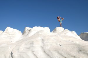 Person standing on white rock formation against a blue sky.