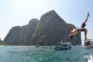 A person performing a backflip off a boat near a rocky island.