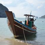 Traditional longtail boat moored on a sandy beach with calm blue waters and hills in the background.