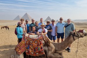 A group of people posing with a camel in the desert.