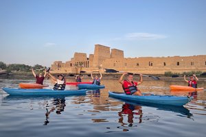 A group of people in kayaks on water with a stone building in the background.