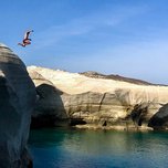 Person cliff diving into a serene blue sea near eroded rock formations.