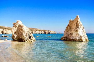 Rocky outcrops along a serene beach with clear blue water and a bright sky.