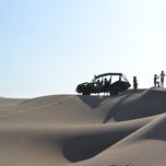 Group of people and a dune buggy on sand dunes under clear skies.