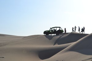 Group of people and a dune buggy on sand dunes under clear skies.