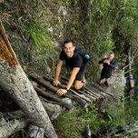 Show thumbnail preview	 Three hikers ascending a steep trail with makeshift log stairs in a forested area.