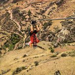 Person ziplining above scenic landscape with terraced fields.