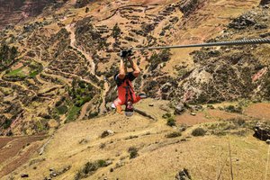 Person ziplining above scenic landscape with terraced fields.