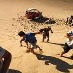 People climbing up a sand dune near a parked dune buggy.