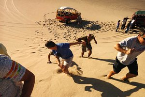 People climbing up a sand dune near a parked dune buggy.