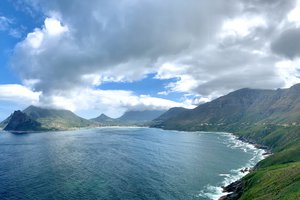 A panoramic view of a coastal landscape with mountains, sea, and clouds.