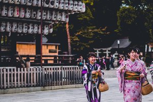Three individuals in traditional japanese kimonos walking past a display of lanterns.