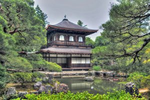 Traditional japanese pavilion surrounded by lush greenery and a tranquil pond.