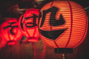 A row of glowing red paper lanterns with japanese characters hanging in a dim setting.