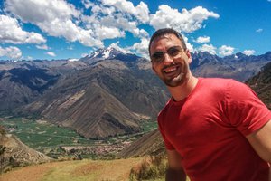 A man in a red shirt standing in front of a mountain.