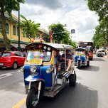 Colorful tuk-tuks transporting passengers on a bustling city street.