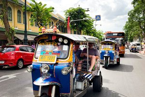 Colorful tuk-tuks transporting passengers on a bustling city street.